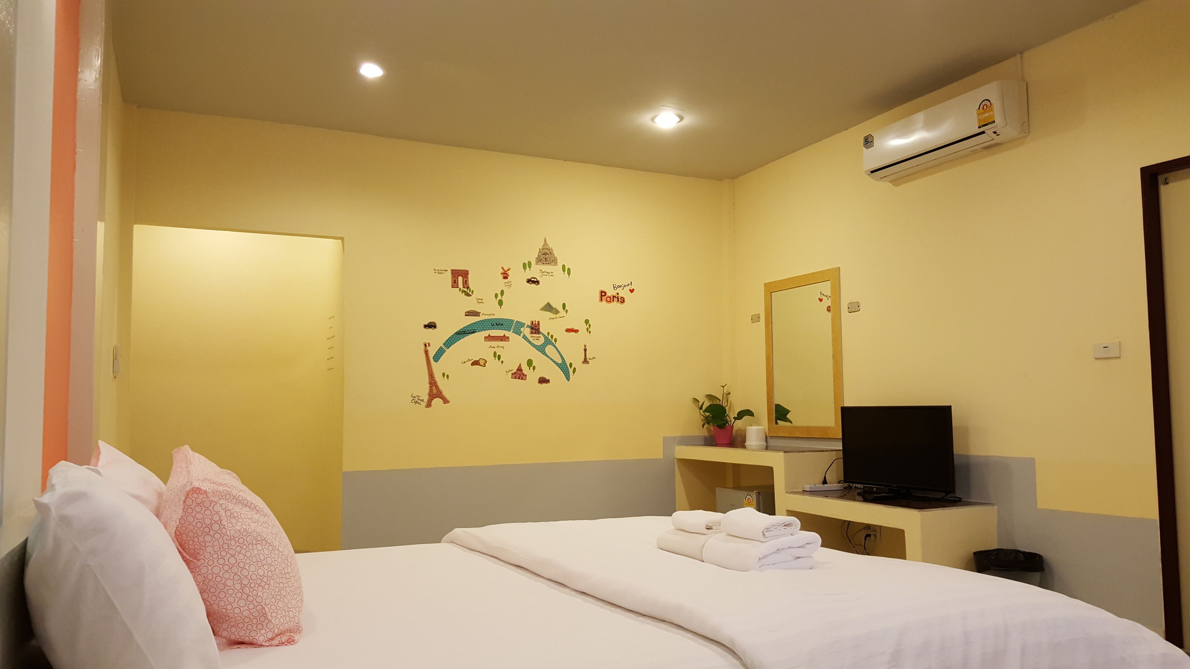 Habitación de hotel con cama, escritorio con televisor, espejo y un adorno de pared con monumentos de París.