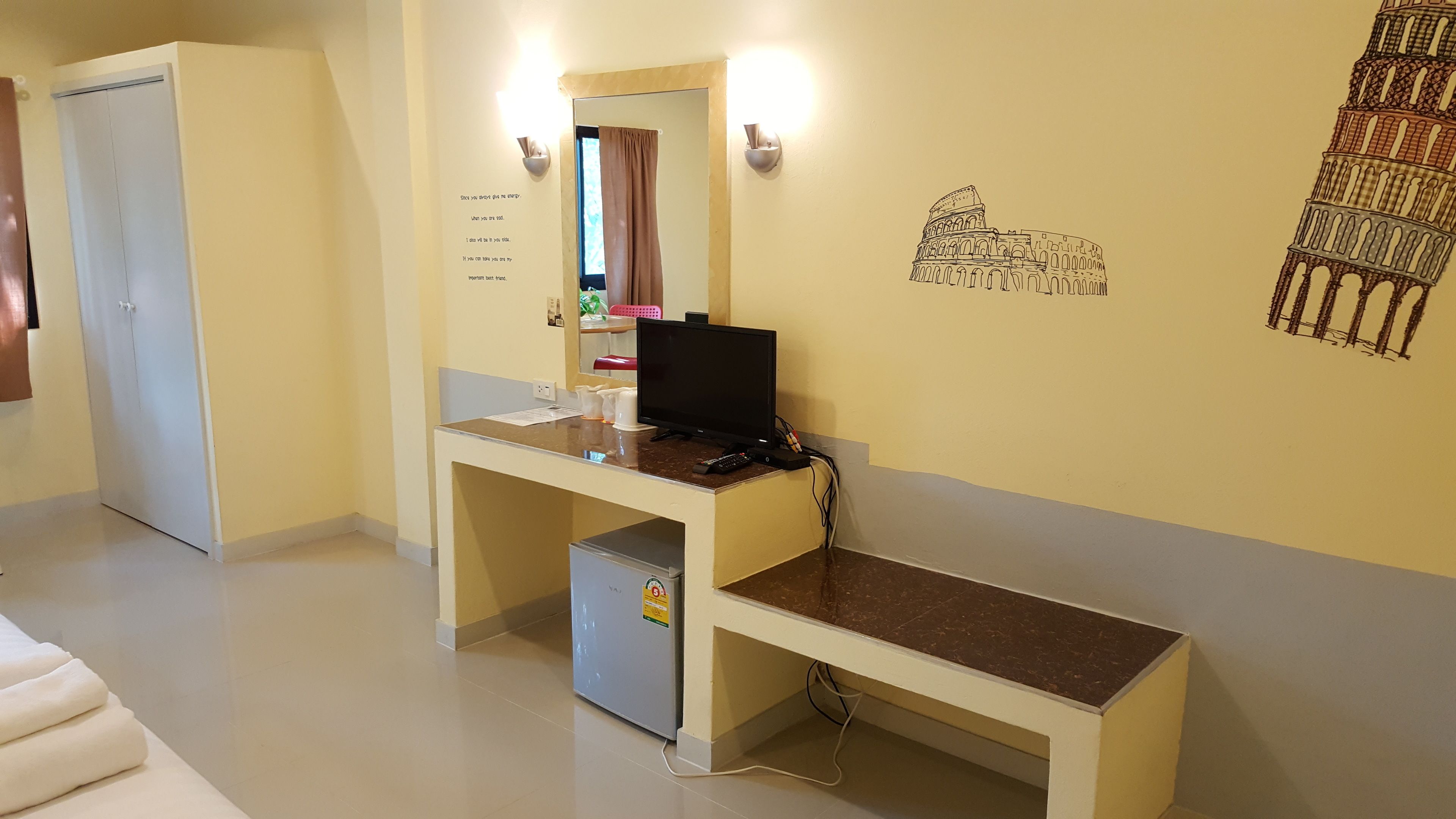 Habitación de hotel con escritorio, refrigerador pequeño, espejo y un cuadro del Coliseo.