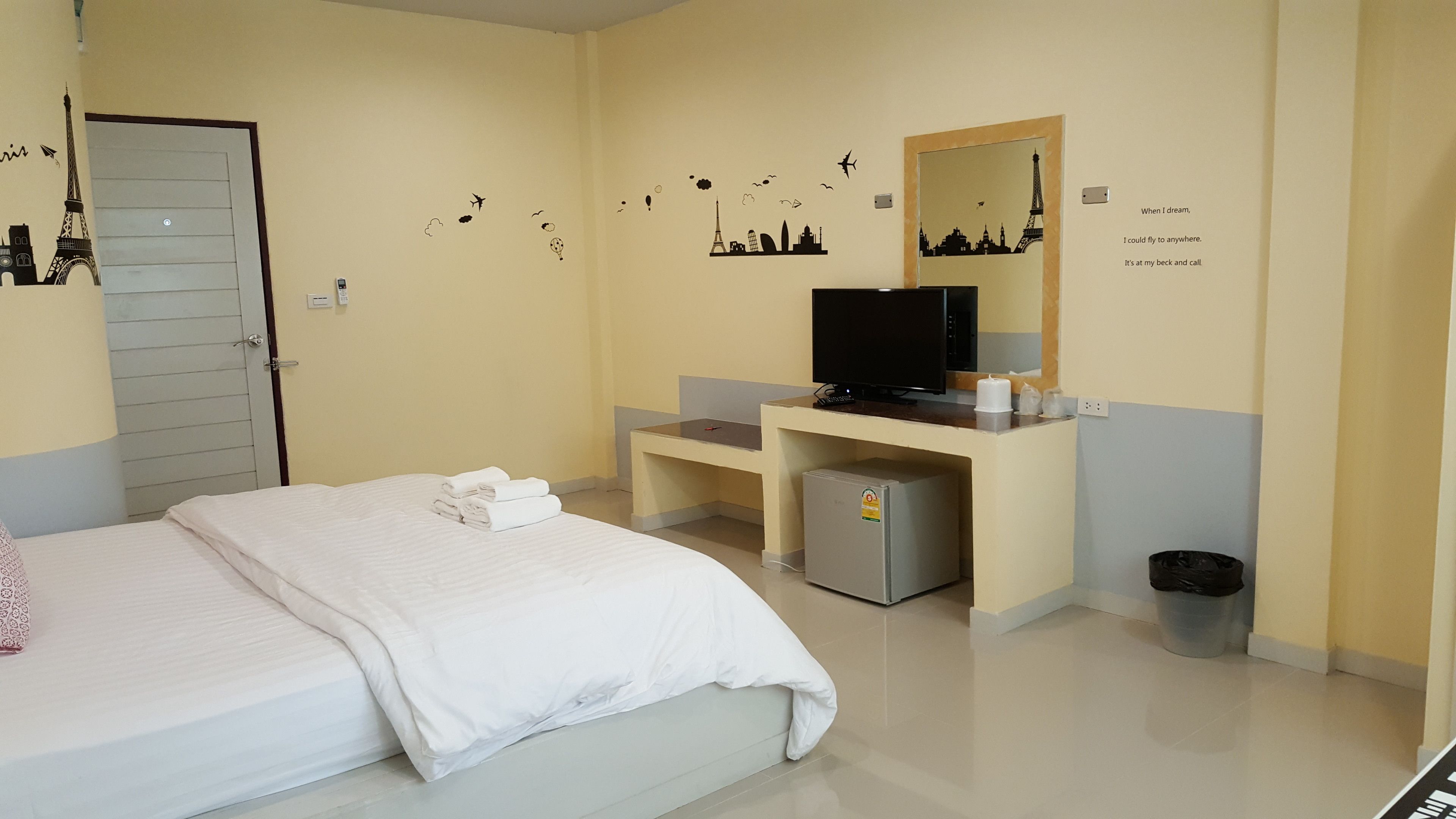 A hotel room with a bed, a desk with a computer, a television, and a small refrigerator.