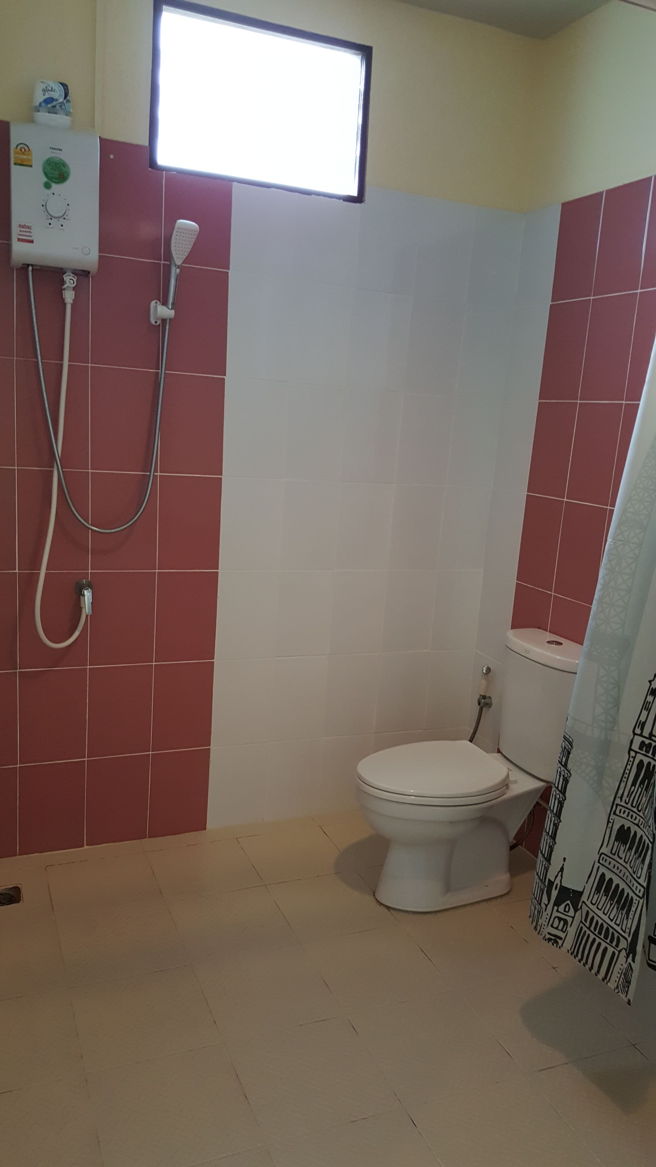 Een badkamer met toilet, douche en raam.