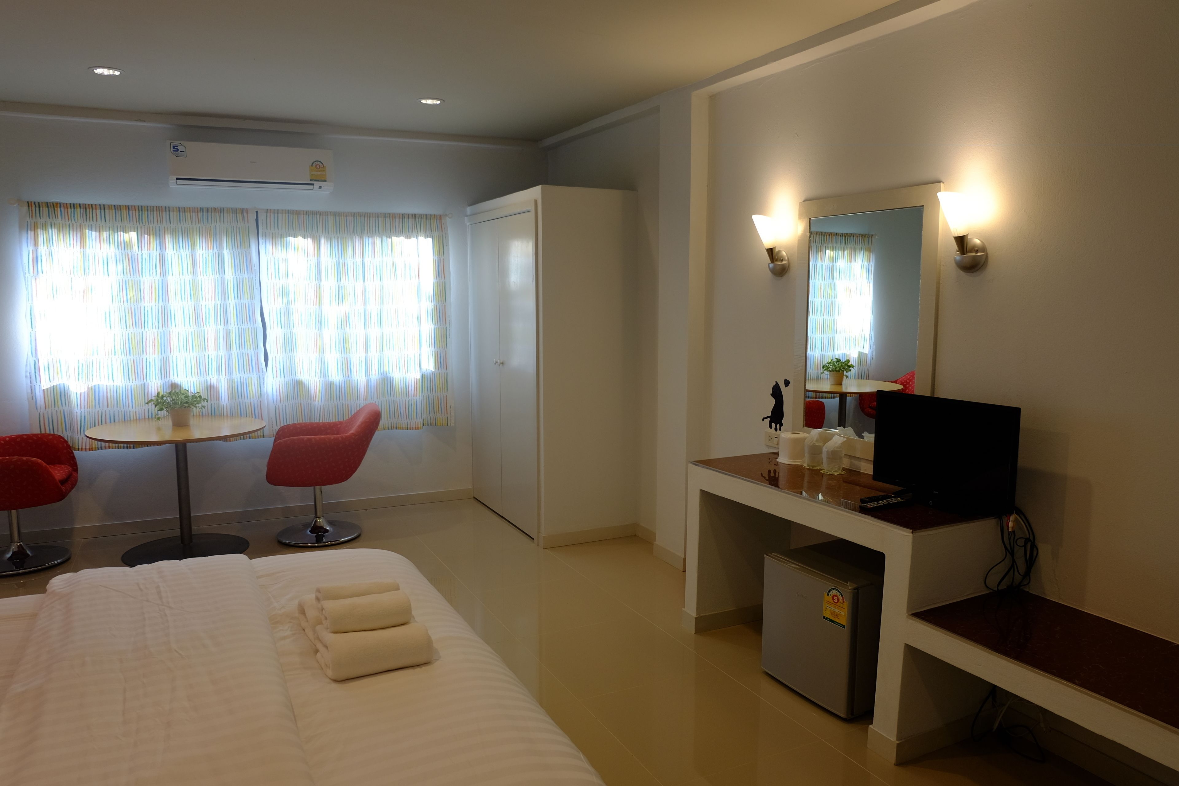 Une chambre d’hôtel avec un lit, un bureau avec une télévision, un petit réfrigérateur et un miroir.