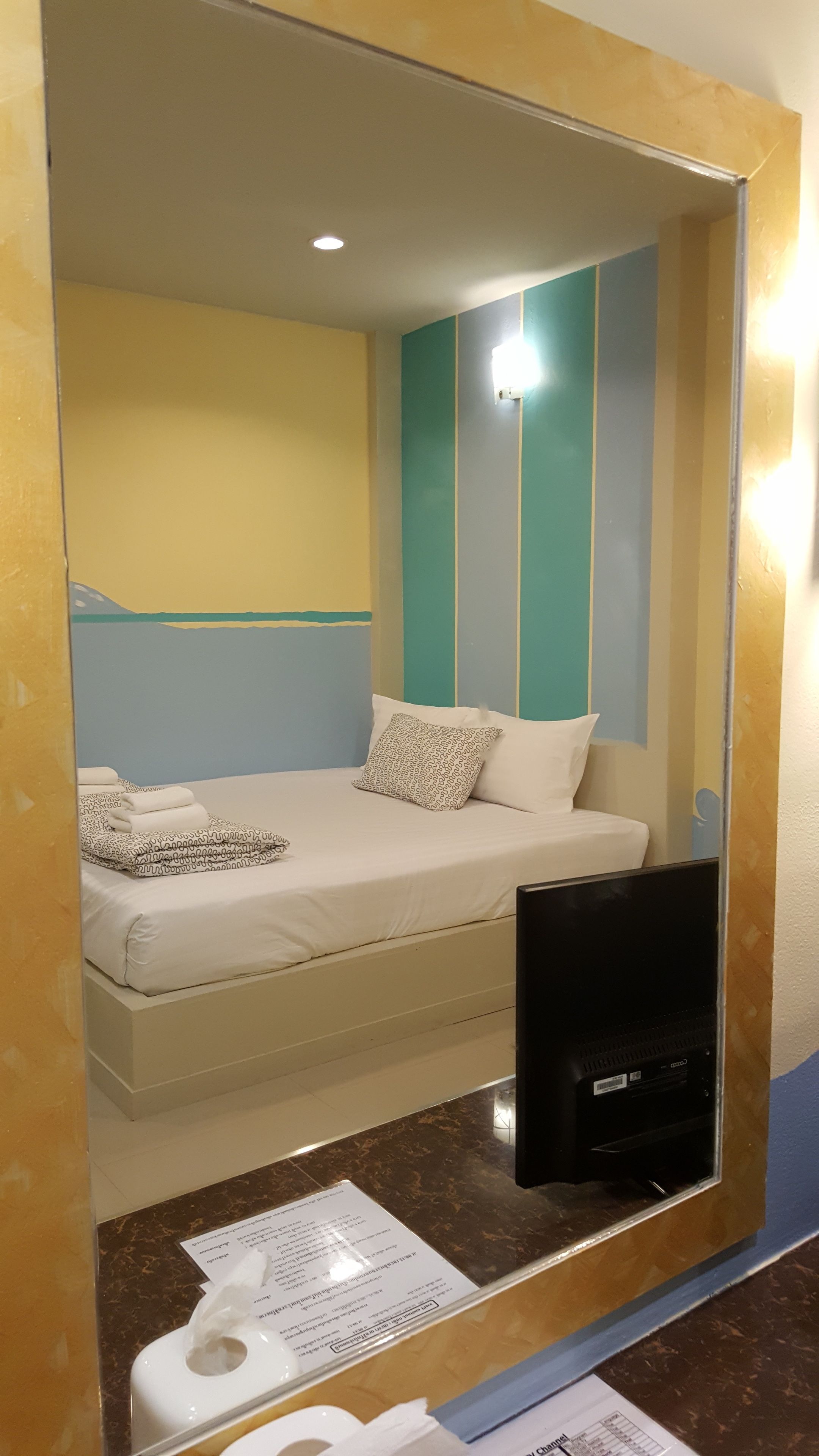 A hotel room with a bed, a television, and a mirror reflecting the room.