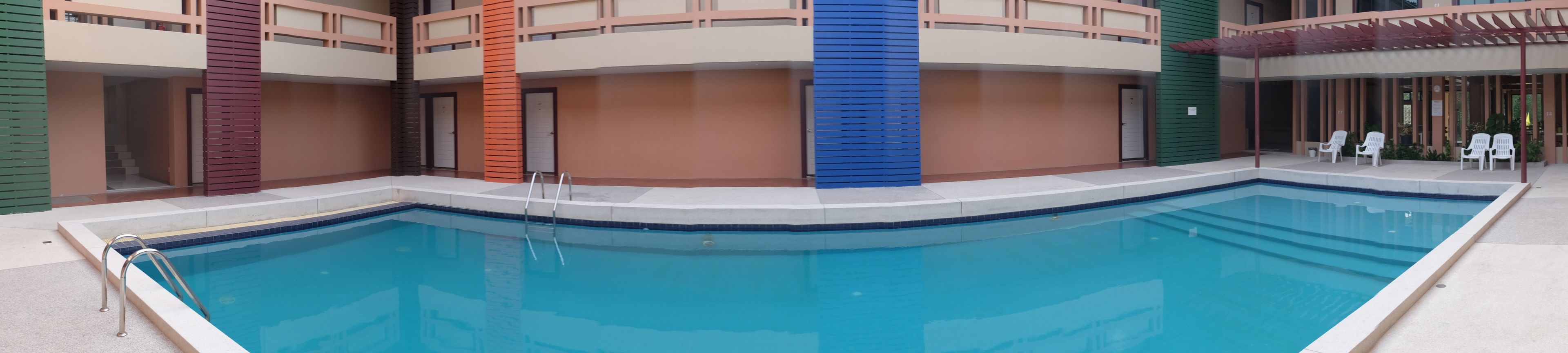 Une piscine à l’eau d’un bleu cristallin, entourée d’un immeuble à étages et doté de balcons.