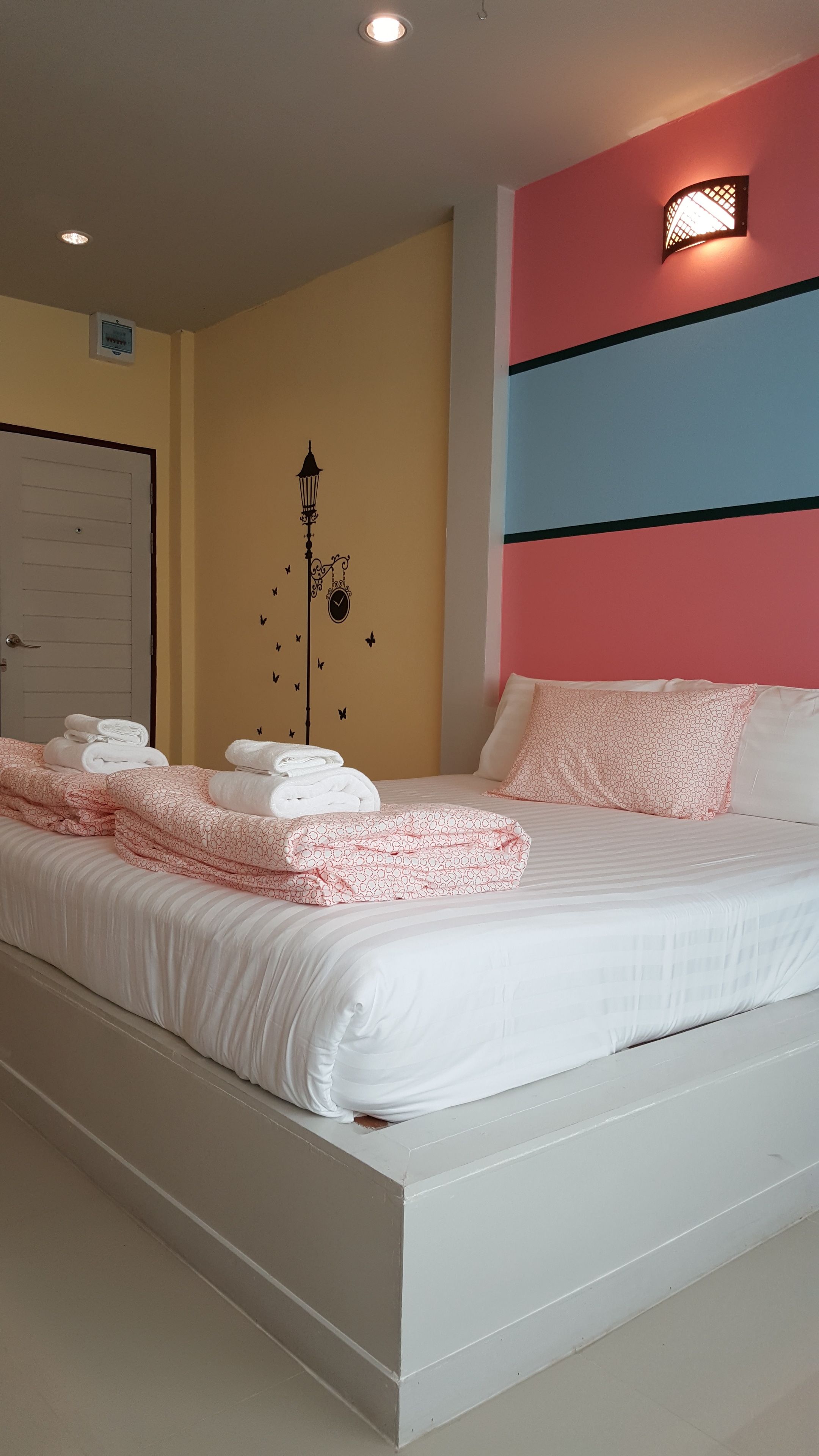 A neatly made bed with folded towels, a wall clock, and a decorative wall light.