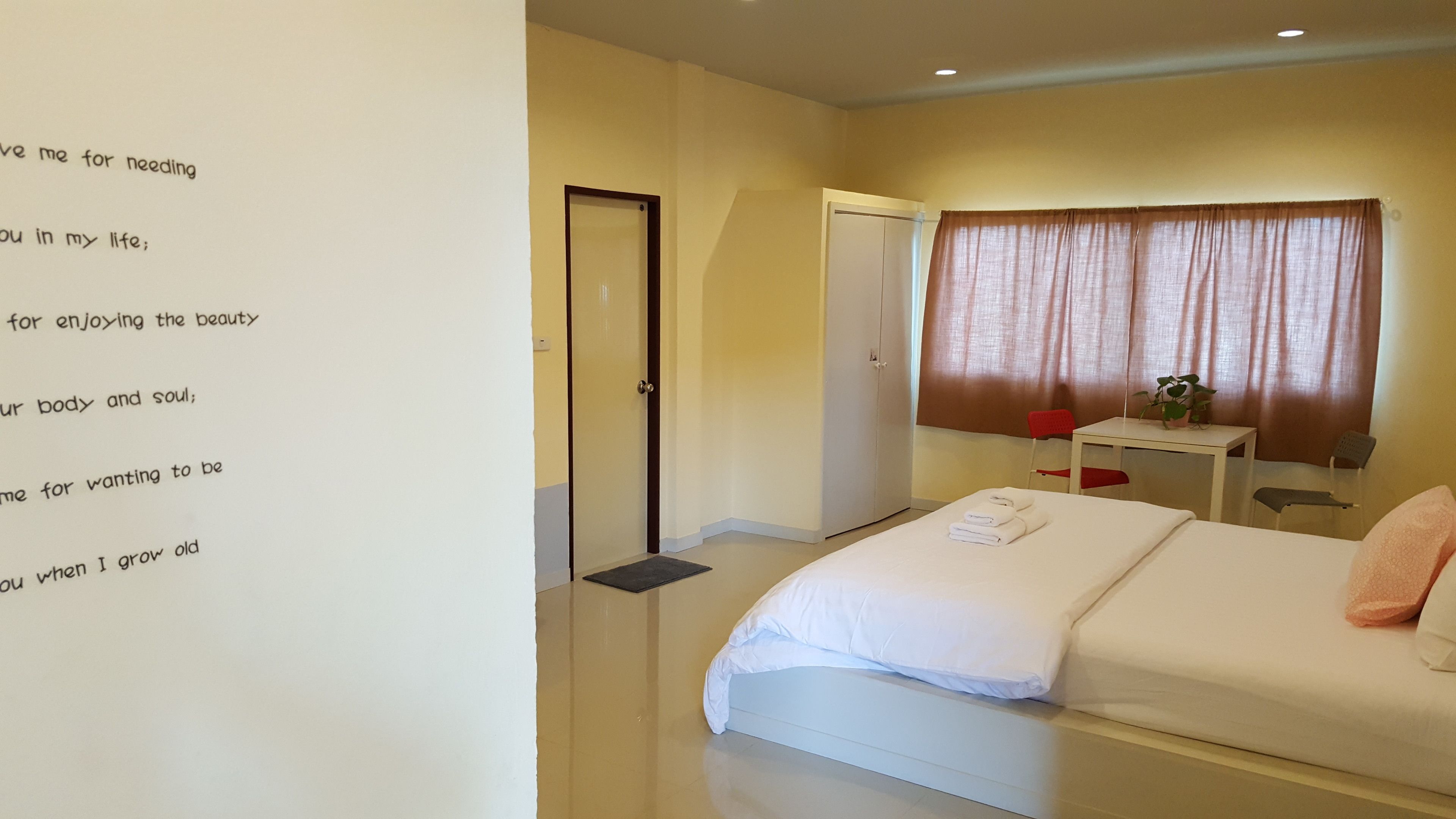 Habitación de hotel con cama, escritorio, silla, ventana con cortinas y pared con texto.