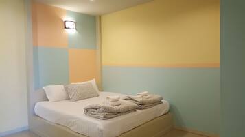 A neatly made bed with patterned pillows and a folded towel, set against a wall with a geometric color scheme.