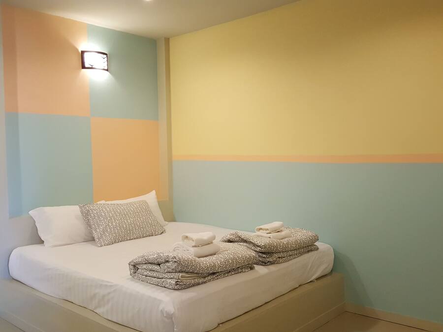 A neatly made bed with patterned pillows and a folded towel, set against a wall with a geometric color scheme.