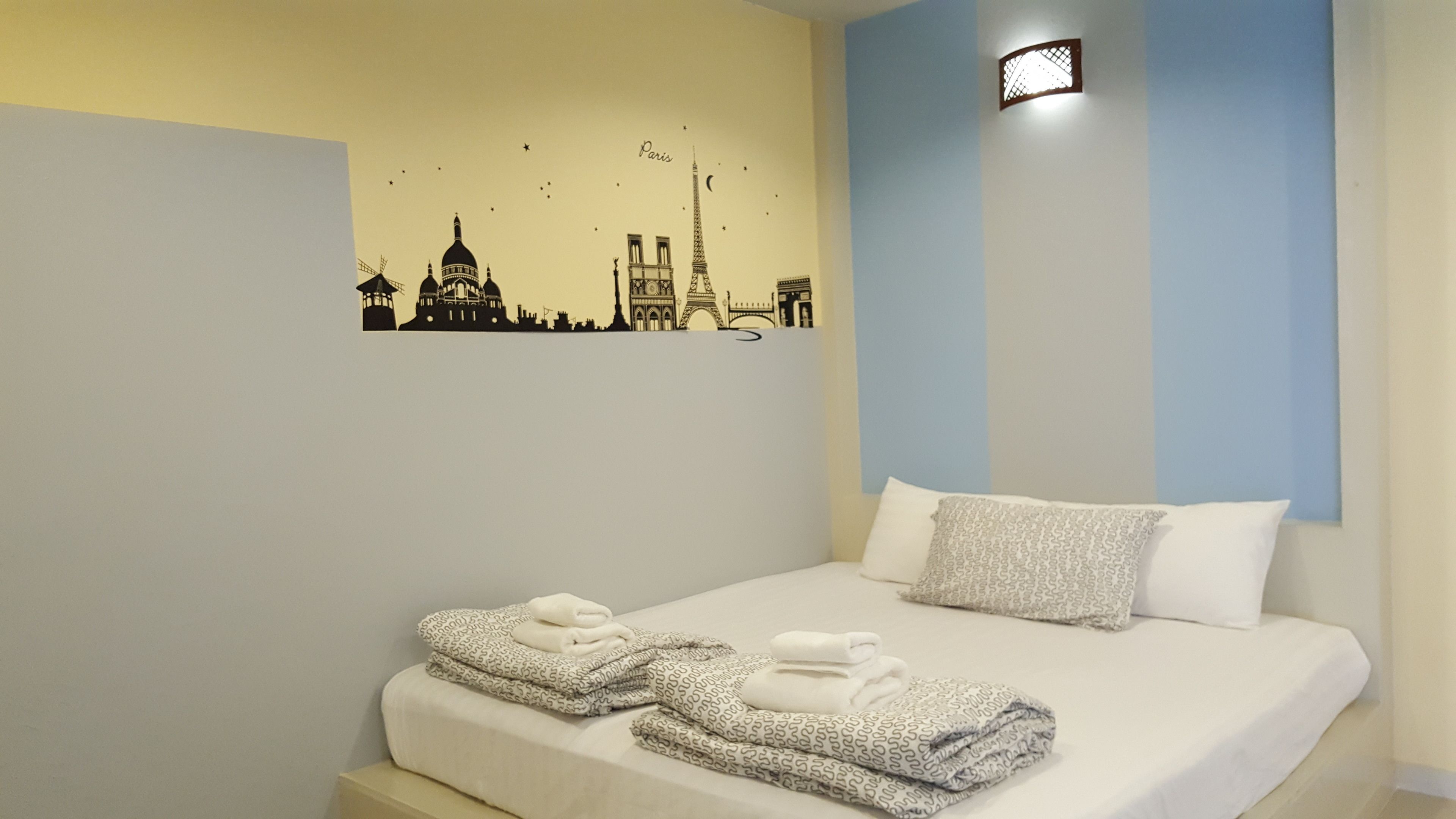 A hotel room with a bed, pillows, and a wall decal of Paris landmarks.