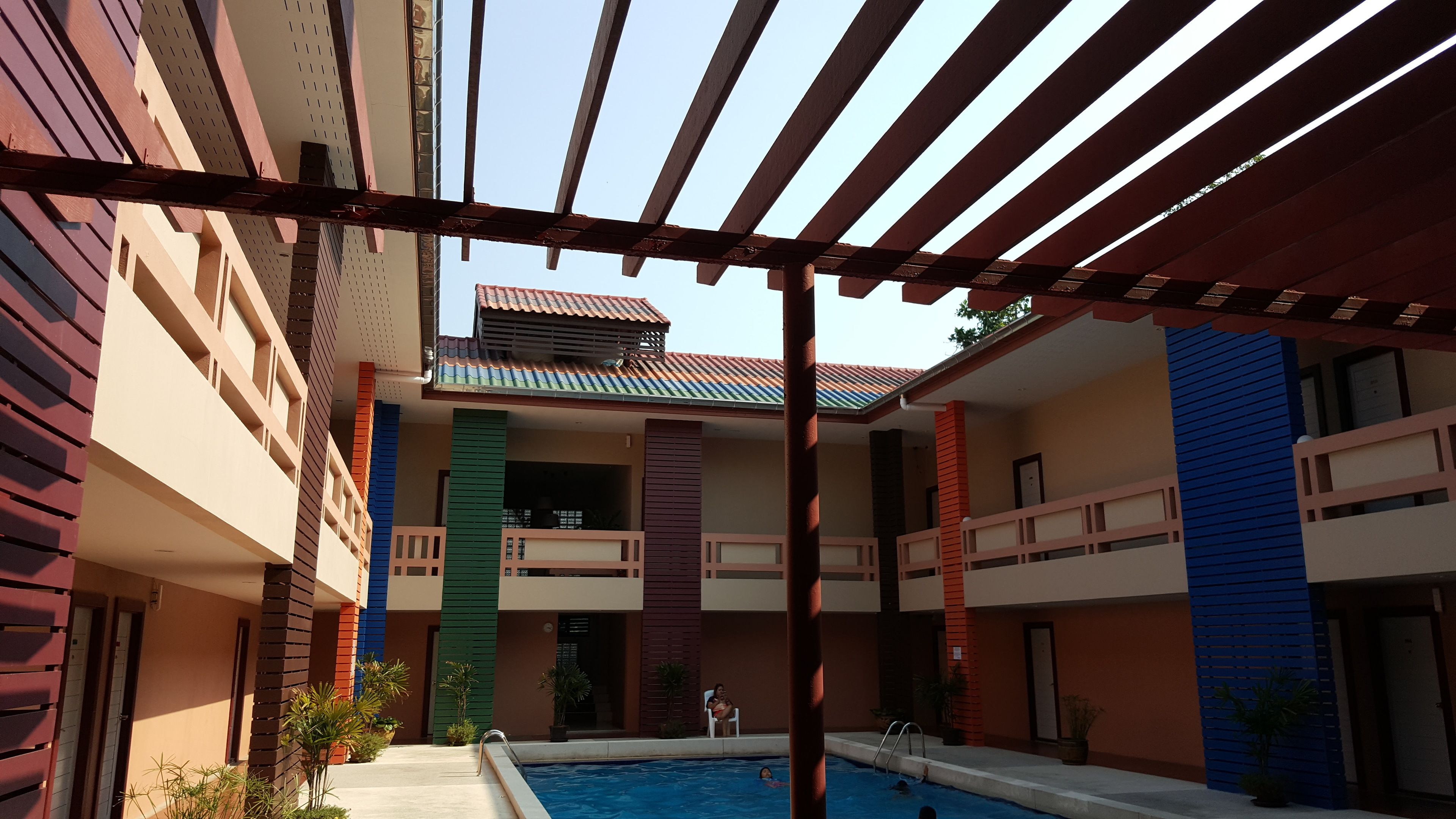 A multi-level building with a swimming pool, balconies, and a covered patio area.