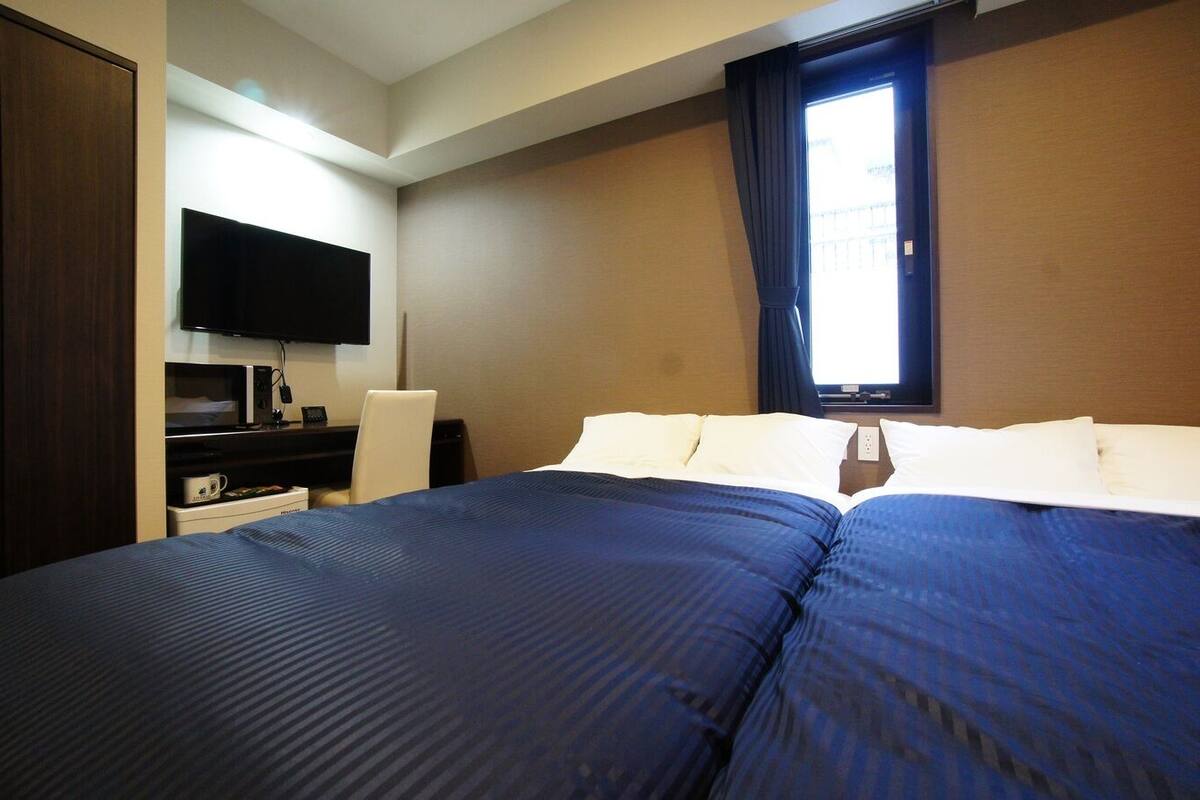 A hotel room with a large bed, a desk with a flat-screen TV, and a window with curtains.