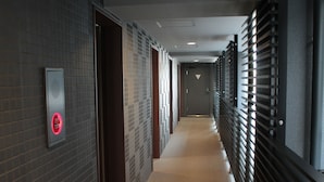 A corridor with a tiled wall, a fire alarm, and a metal railing. - Hotel Livemax Tokyo Bakurocho (Tokyo)