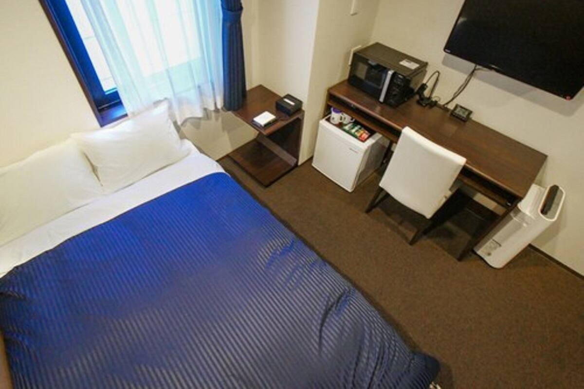 A hotel room with a bed, a desk with a computer, a microwave, and a TV.