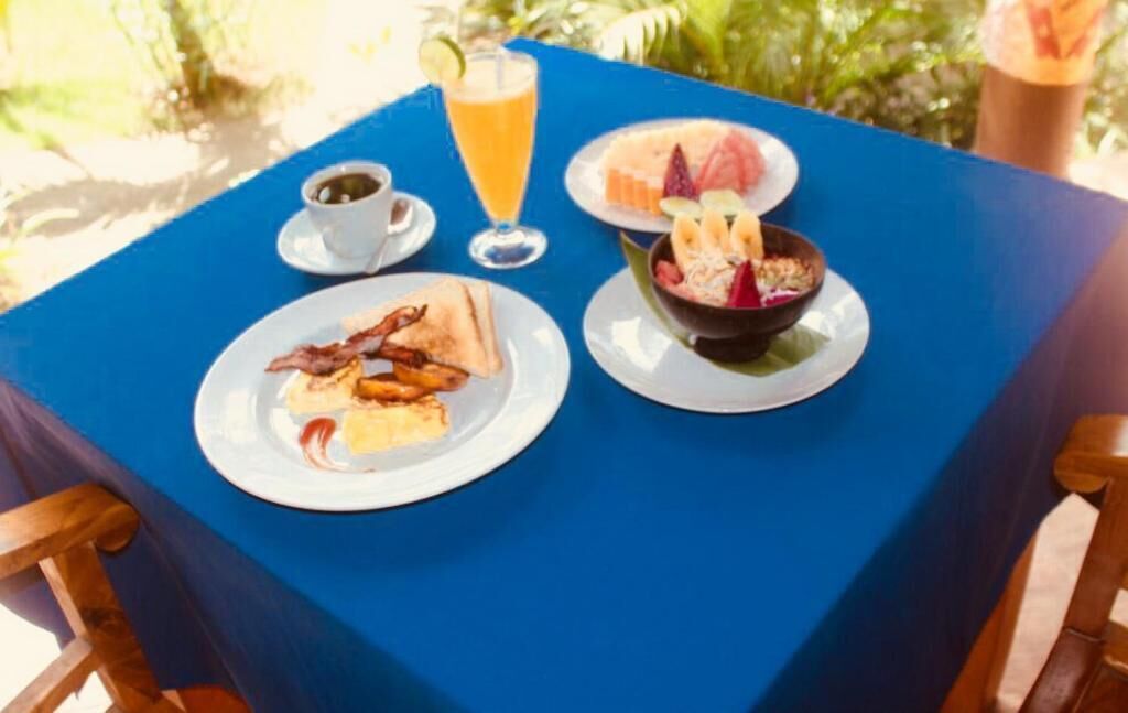 A table with breakfast items including toast, bacon, a bowl of fruit, a glass of orange juice, and a cup of coffee.