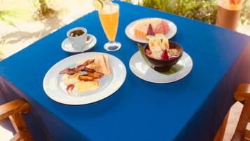 A table with breakfast items including toast, bacon, a bowl of fruit, a glass of orange juice, and a cup of coffee.