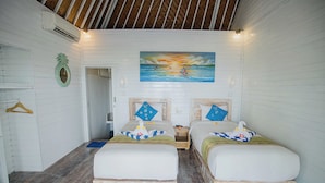 Ein Zimmer mit zwei Betten, einem Gemälde, das einen Sonnenuntergang über dem Meer zeigt, und einer Holzzahlendecke.