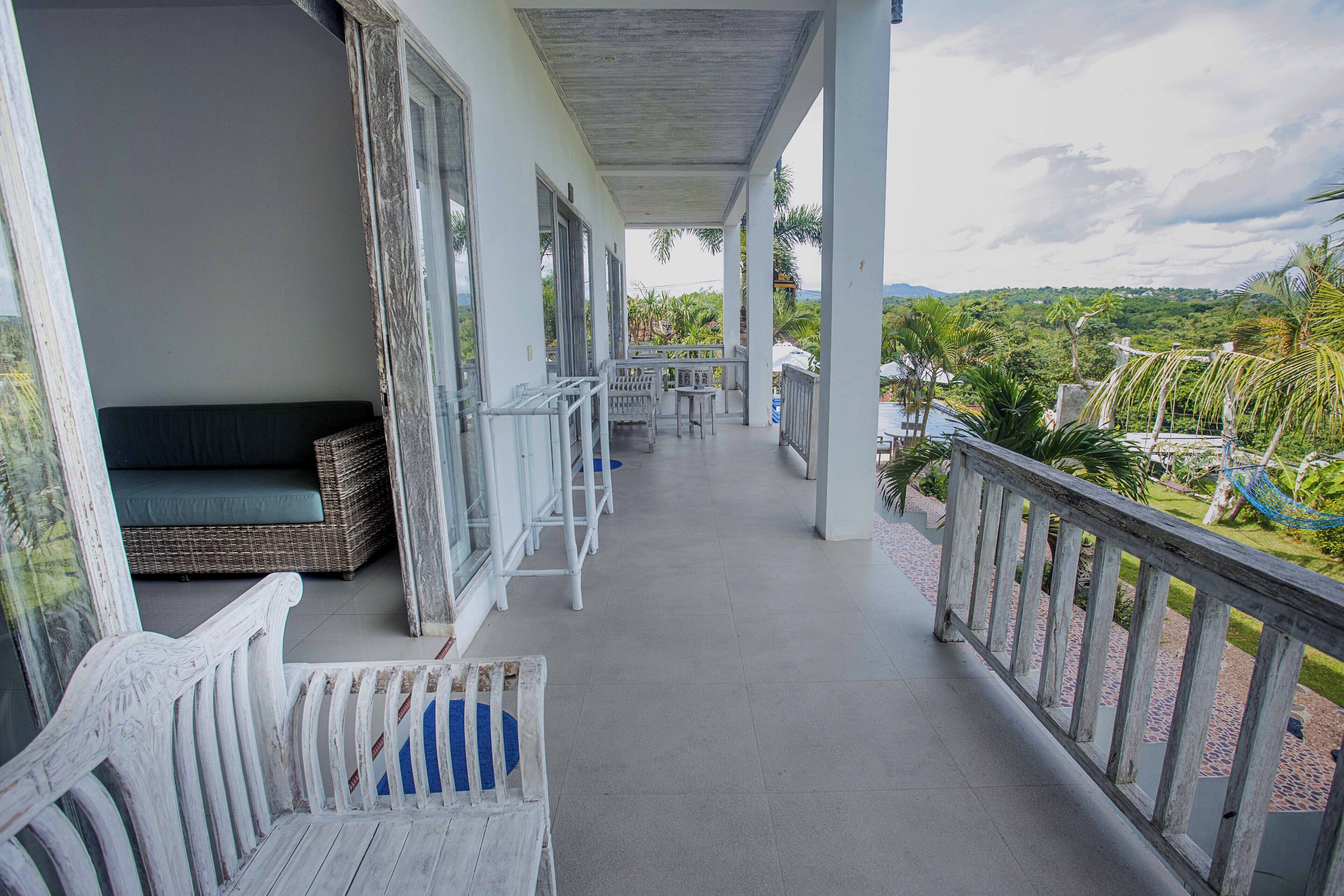 A covered balcony with wicker furniture, a view of a lush landscape, and a clear sky.