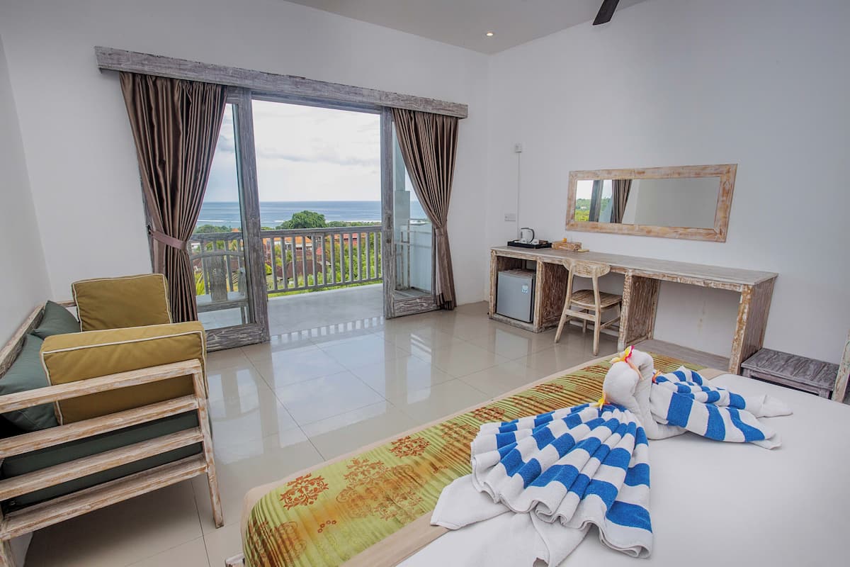 Une chambre d’hôtel équipée d’un lit, d’un bureau, d’une chaise et offrant une vue sur la mer grâce à de grandes fenêtres.