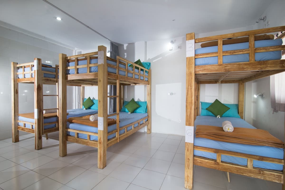 Une chambre avec trois lits superposés, chacun étant muni d’une étiquette numérotée, d’une structure en bois et de draps bleus.