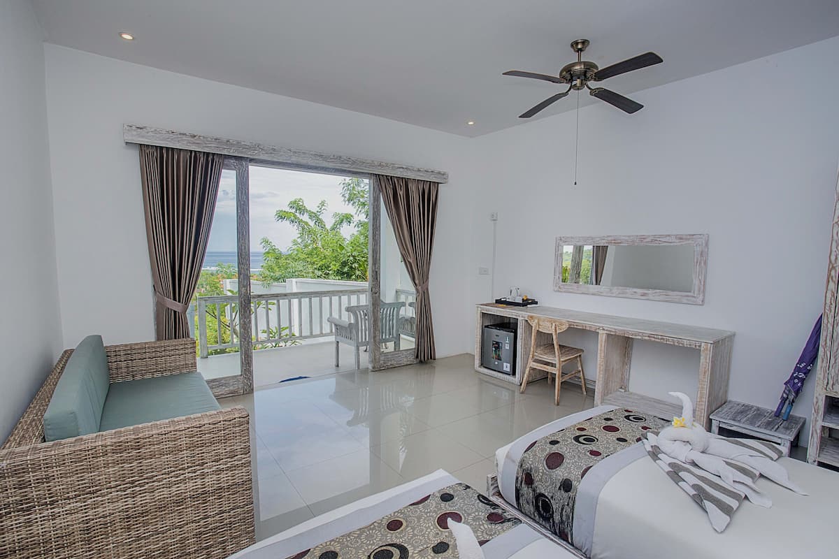 Une chambre d’hôtel avec un balcon, un bureau, un lit et un ventilateur de plafond.