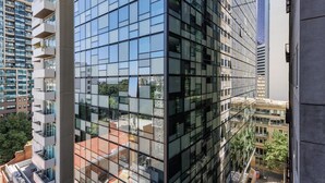A modern high-rise building with reflective glass windows, multiple balconies, and a view of surrounding urban structures. - Avani Melbourne Jazz Corner Residences (Melbourne)