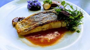 Um prato com peixe grelhado, um pouco de molho e alguns acompanhamentos.