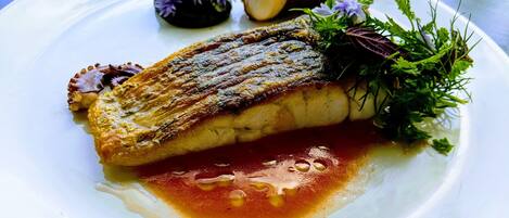 Ein Teller mit gegrilltem Fisch, einer kleinen Soßenmenge und einigen Garnituren.