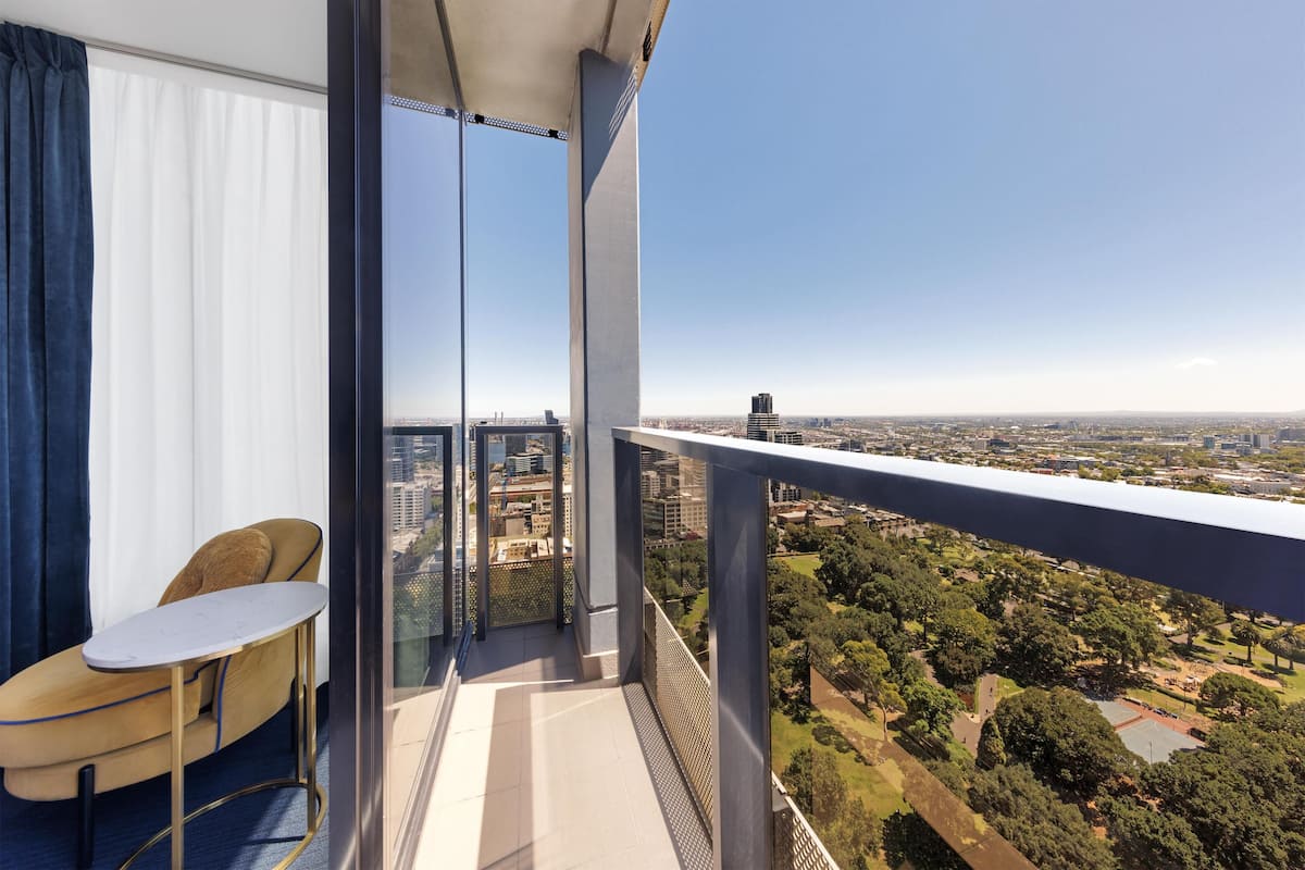A balcony with a table and chair, offering a view of a cityscape and a park.