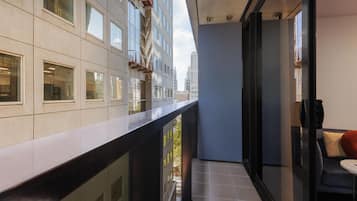 Un balcón moderno con vistas a la ciudad, una puerta de vidrio que da a una habitación y una pequeña mesa con una silla.