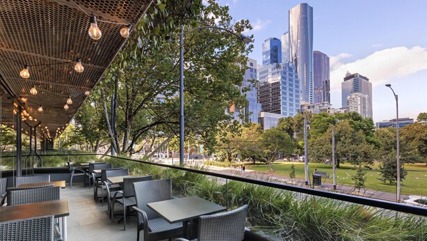 An outdoor patio with wicker furniture and hanging lights, overlooking a cityscape with modern buildings. - Avani Melbourne Jazz Corner Residences (Melbourne)