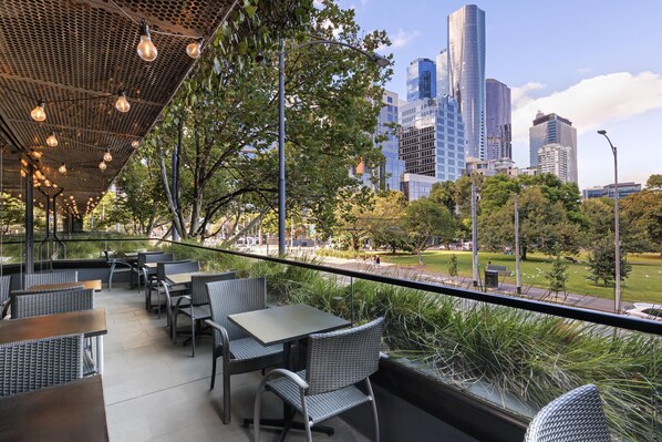 Uma área externa com mesas e cadeiras, com vista para um horizonte urbano com edifícios modernos.