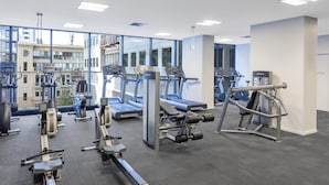 Uma academia com equipamentos de cardio, máquinas de peso e um espelho grande.