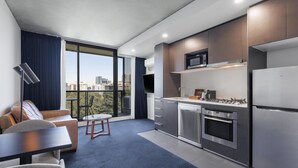 A modern kitchen with a built-in oven and microwave, a dining area with a table and chairs, and a large window offering a city view. - Avani Melbourne Jazz Corner Residences (Melbourne)