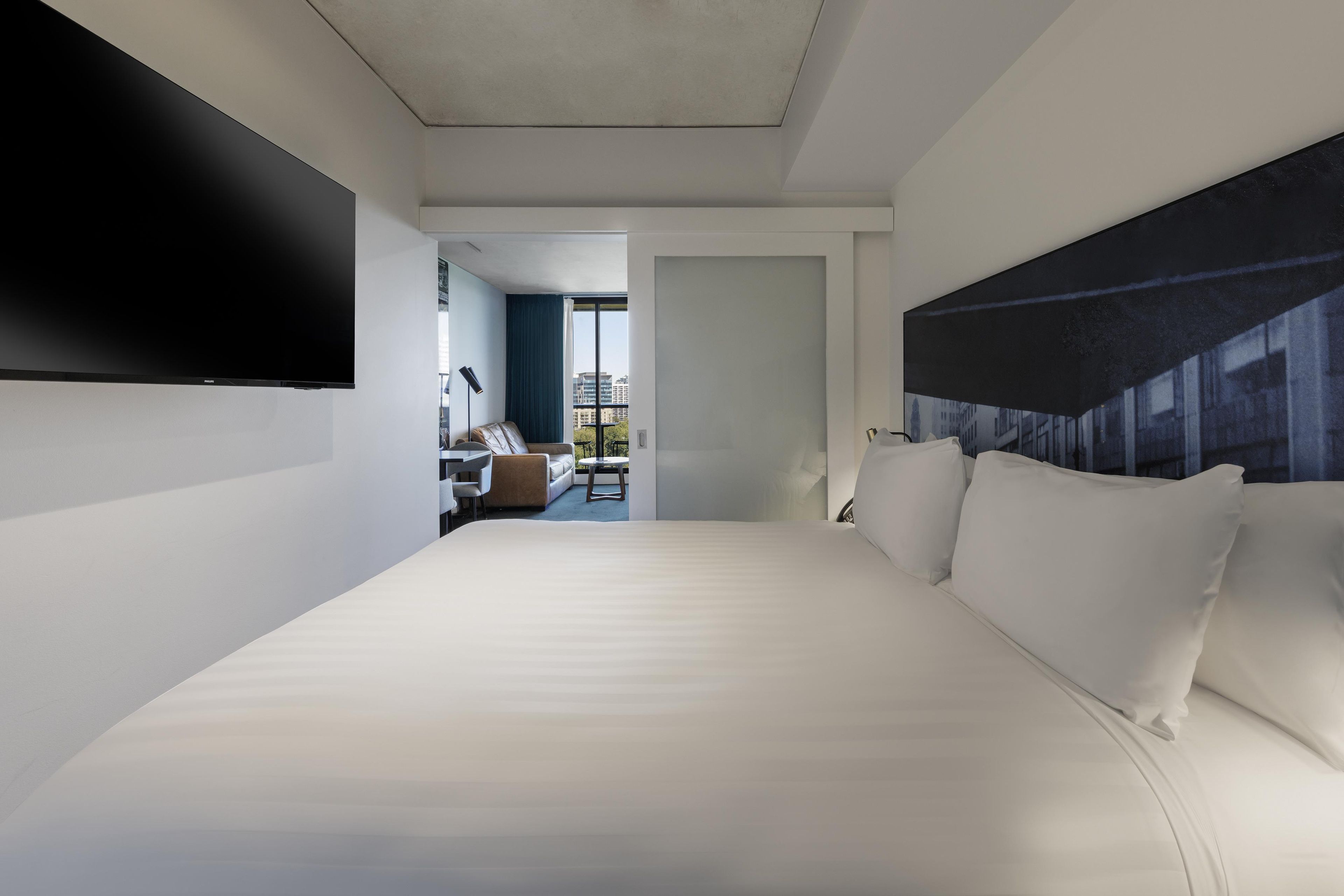 A modern hotel room with a large bed, a flat-screen TV, and a view of the city through the window.