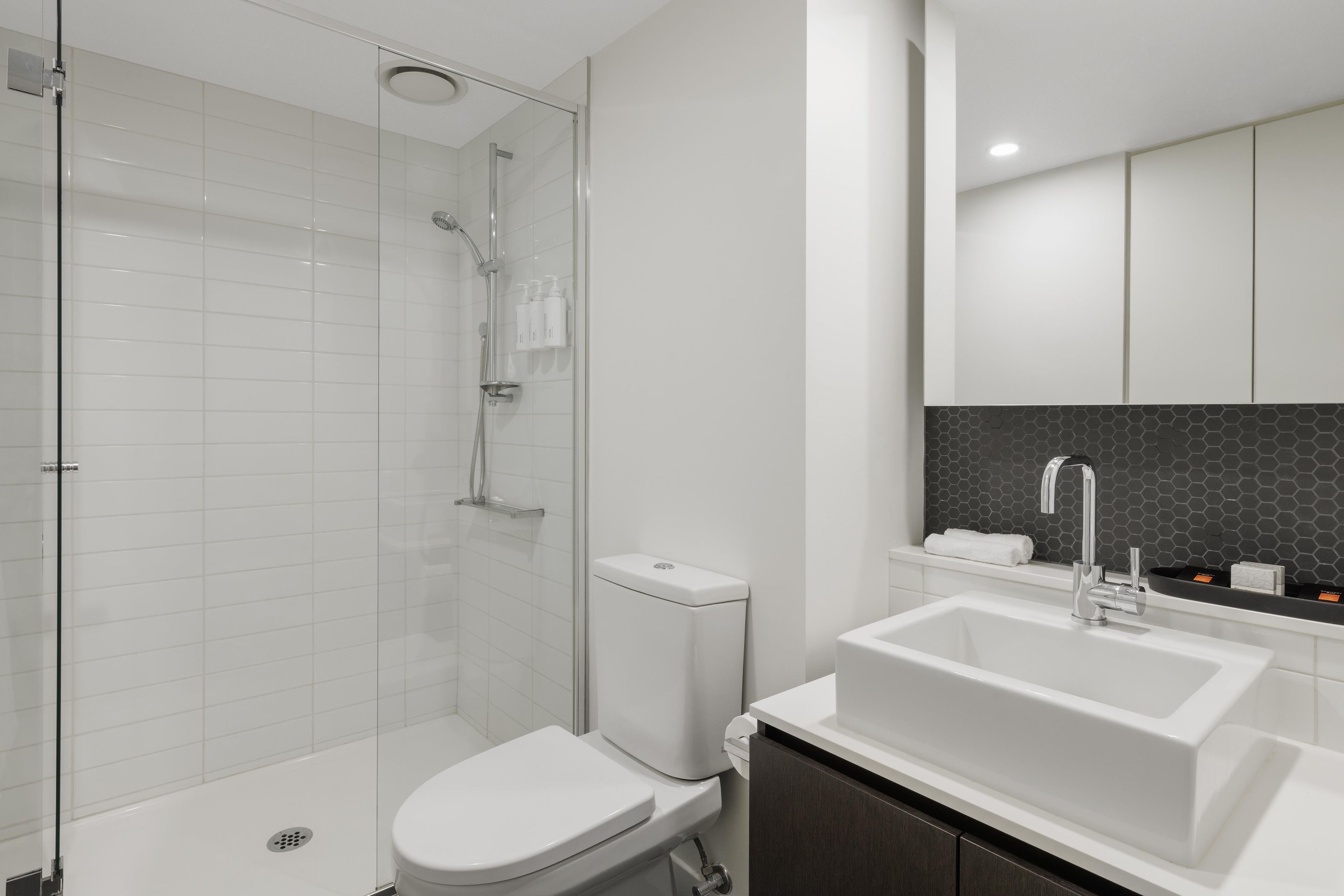 Une salle de bain moderne avec une douche à parois de verre, des toilettes blanches, un grand lavabo blanc et un meuble-lavabo en bois foncé.