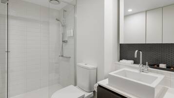 Une salle de bain moderne avec une douche à parois de verre, des toilettes blanches, un grand lavabo blanc et un meuble-lavabo en bois foncé.