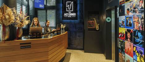 A reception desk with a sign for "The Jazz Corner Hotel," a TV screen, and a wall decorated with movie posters.