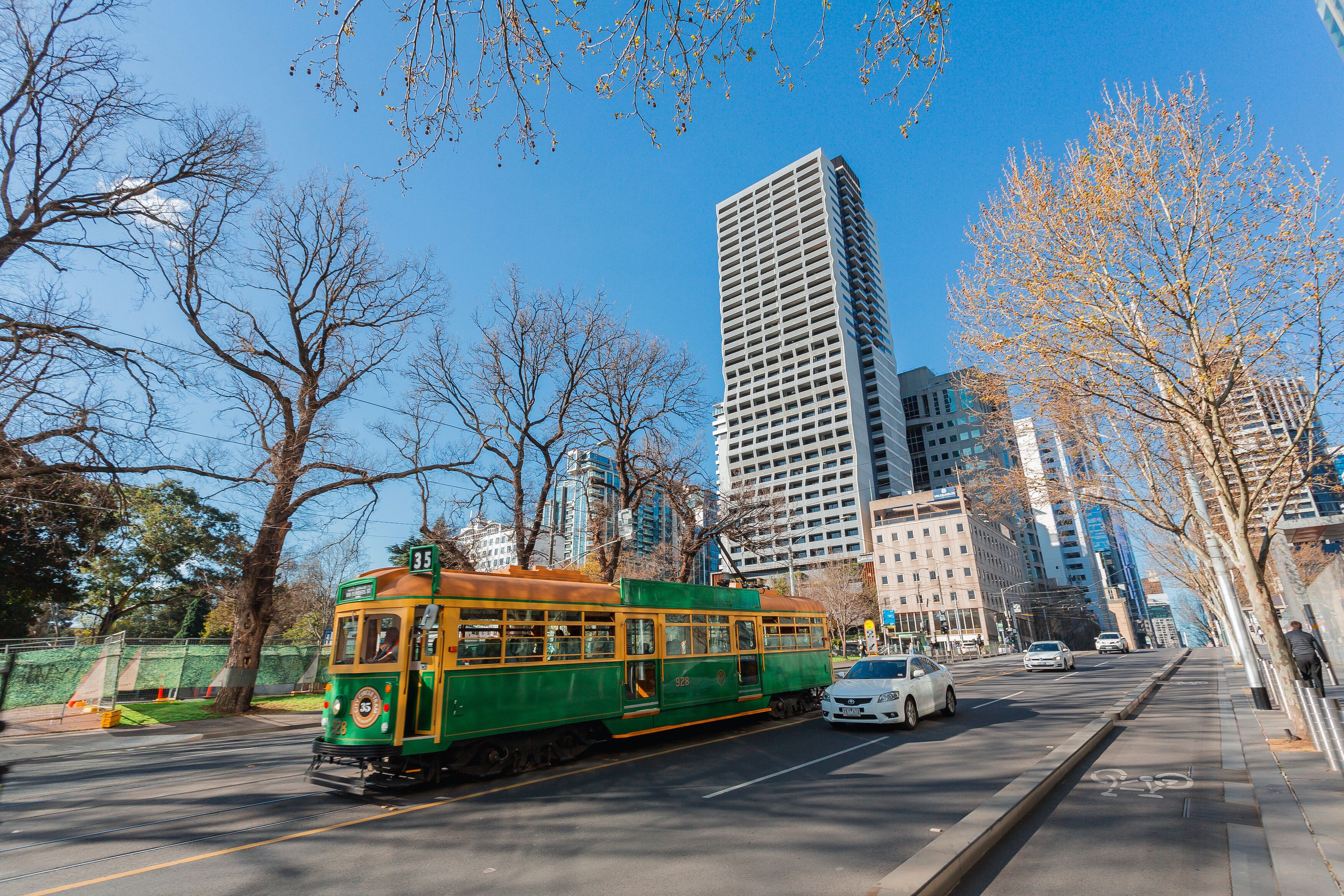 A green and yellow tram on a city street with tall buildings in the background.