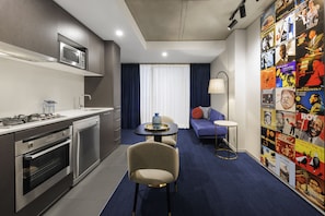 A compact hotel room with a kitchenette, a dining area, and a seating space with a wall of posters. - Avani Melbourne Jazz Corner Residences (Melbourne)