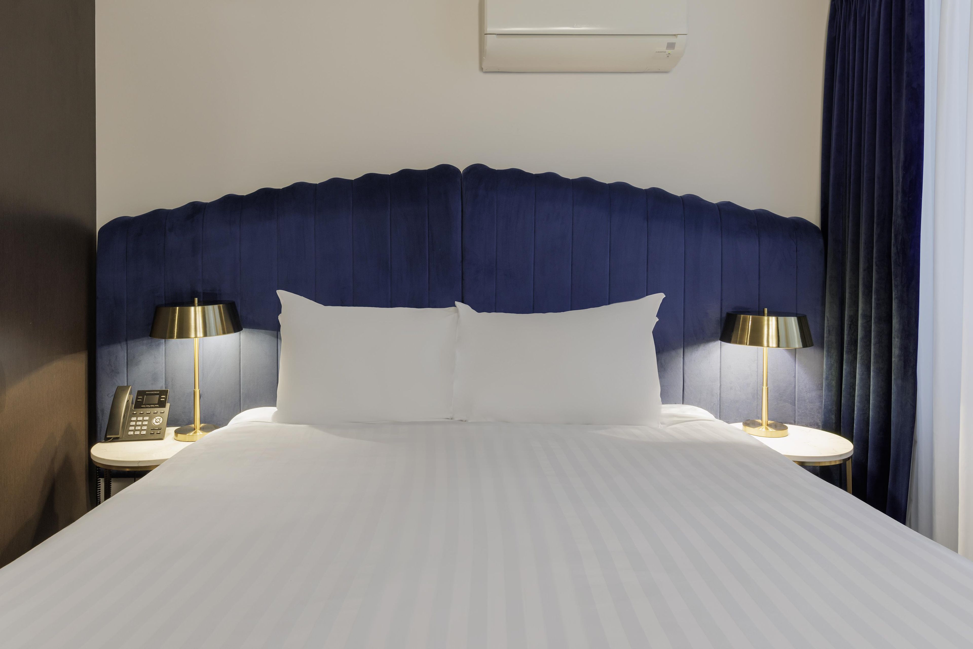 A hotel room with a large bed, two bedside tables with lamps, a telephone, and a wall-mounted air conditioning unit.