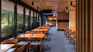 A modern restaurant with wooden tables and chairs, large windows, and a kitchen area visible in the background. - Avani Melbourne Jazz Corner Residences (Melbourne)