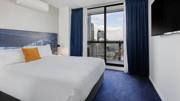 Ett hotellrum med en stor säng, en platt-TV, ett fönster med gardiner och utsikt över staden.