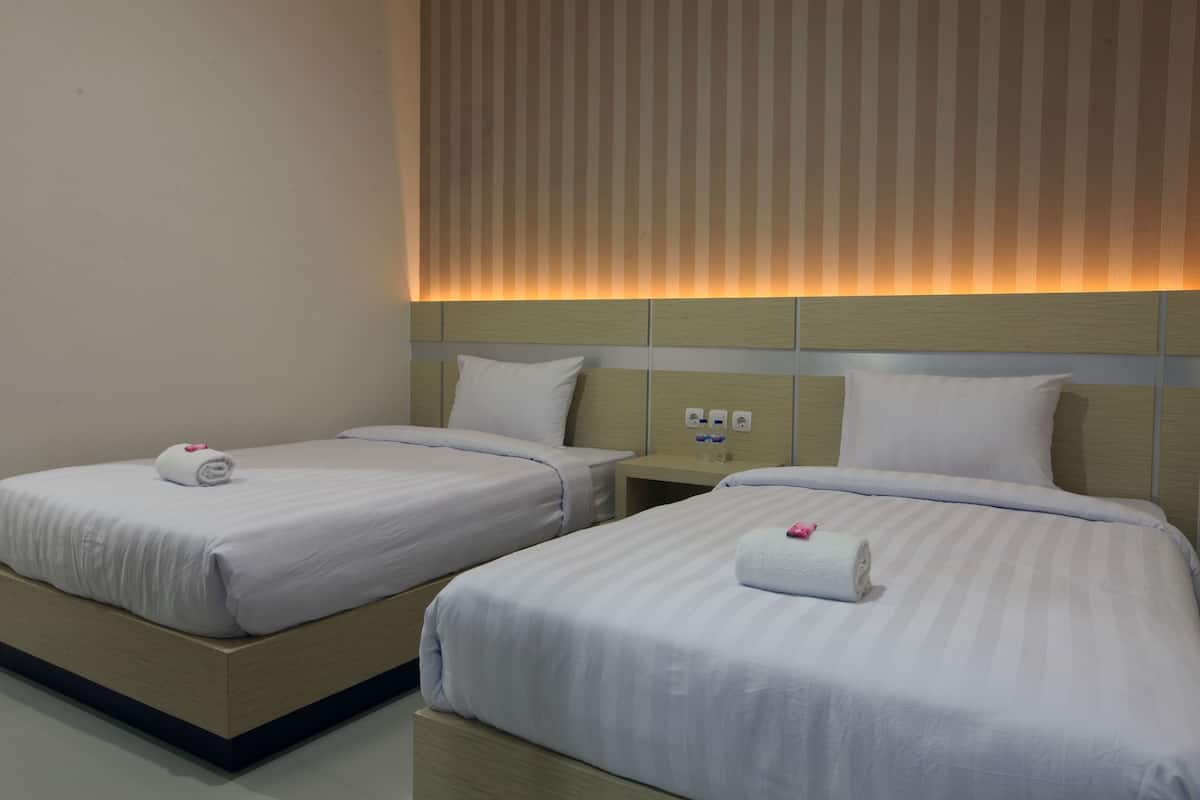 Two single beds with white linens and pillows, a wooden headboard, and a wall-mounted light fixture.