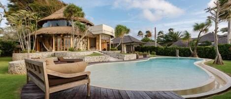 A resort with a swimming pool, wooden deck, and thatched-roof structures.