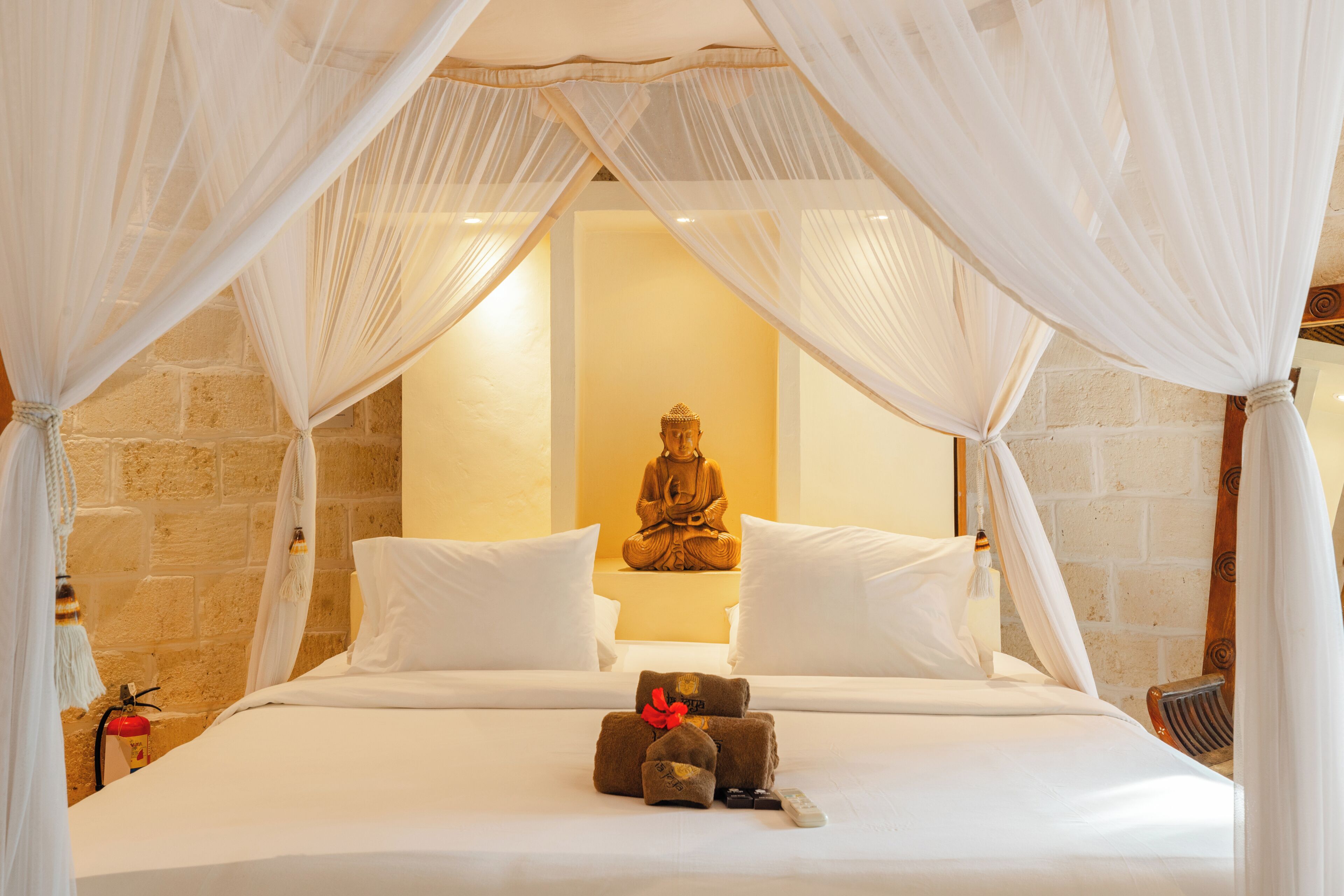 Una cama con dosel, una estatua de Buda y un extintor.