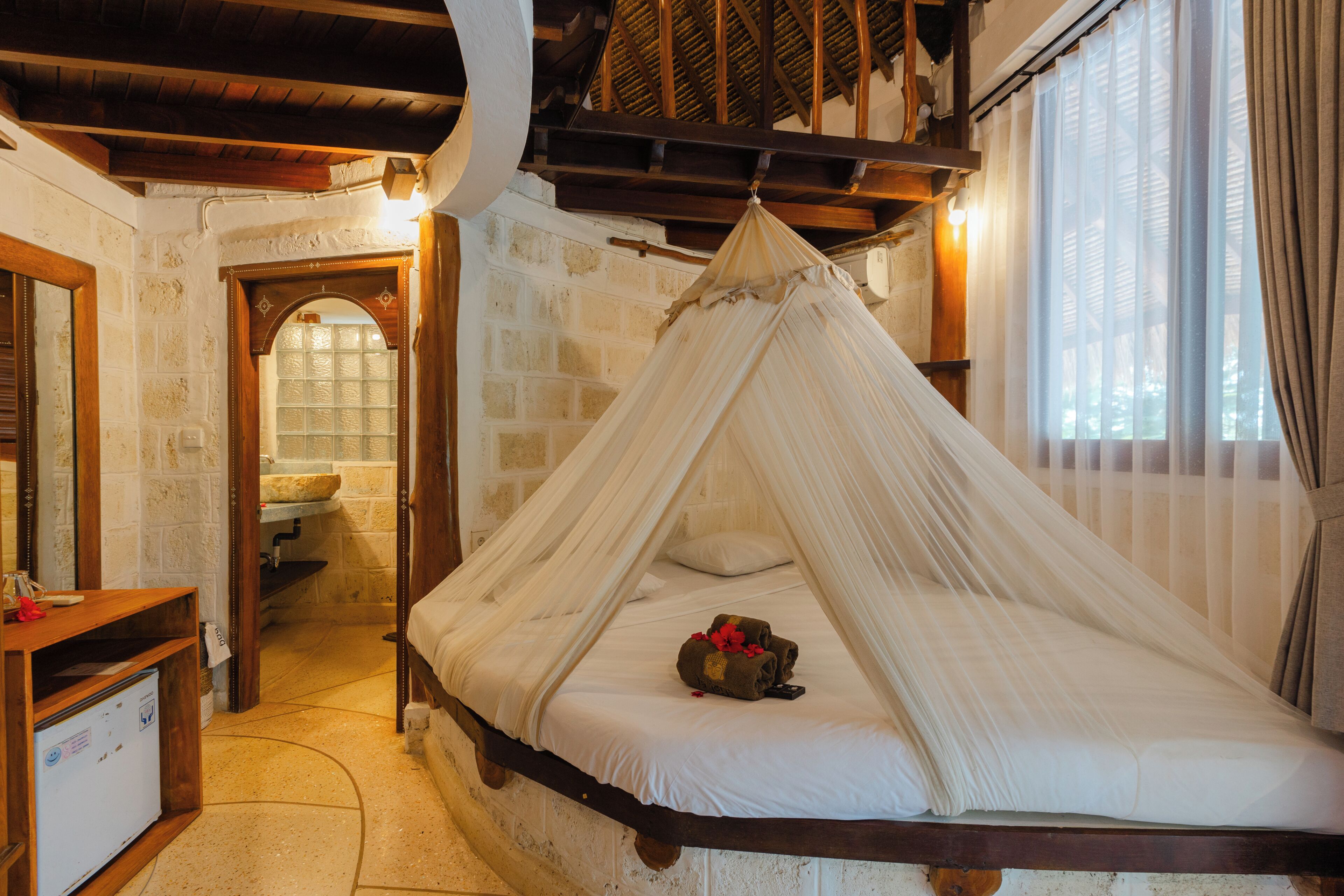 Une chambre avec un lit sous un dais, un bureau en bois et un mur en pierre.