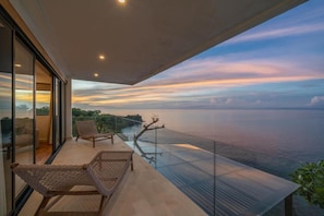 A balcony with a glass railing overlooking a body of water and a sunset.