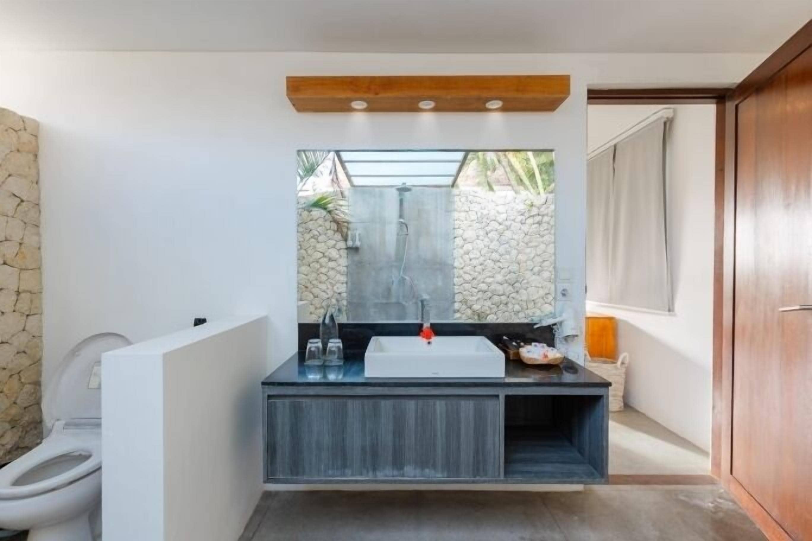 A modern bathroom with a white toilet, a black sink with a red faucet, and a large mirror above it.