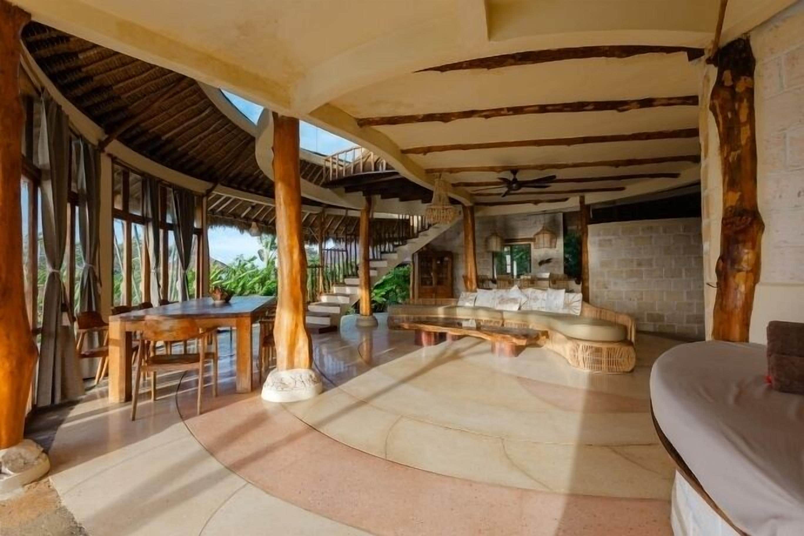 A spacious indoor area with a high ceiling, wooden beams, a dining table, and a seating area with a cushioned bench.