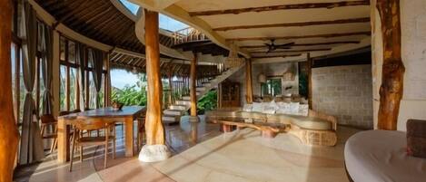 A spacious indoor area with a high ceiling, wooden beams, a dining table, and a seating area with a cushioned bench.