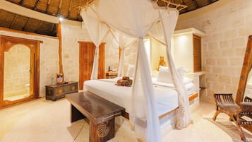 Una habitación con una cama, un banco, una silla de madera, una estatua y un muro de piedra.